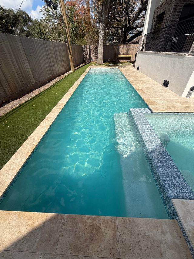 Narrow rectangular pool with sunlit ripples, artificial turf along one side and a tiled spa edge