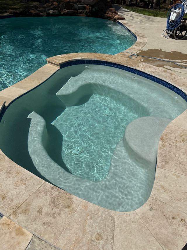 Curved spa with a bench seat and clear water, set into a travertine deck beside the pool