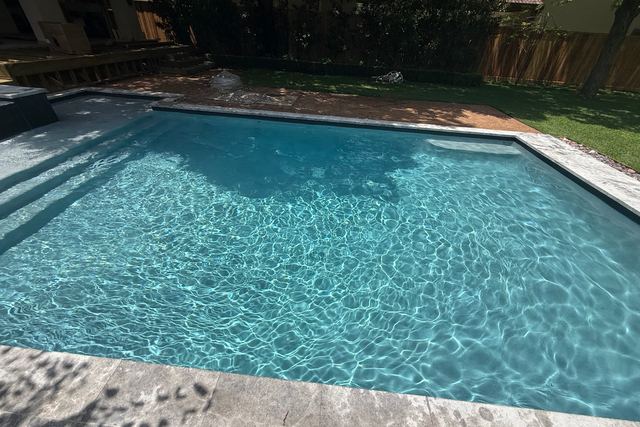 Rectangular pool with clear blue water and a grey stone deck, seen across its full width