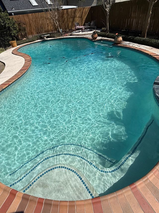 After: the same kidney-shaped pool with brick coping and clear, sparkling water over the steps
